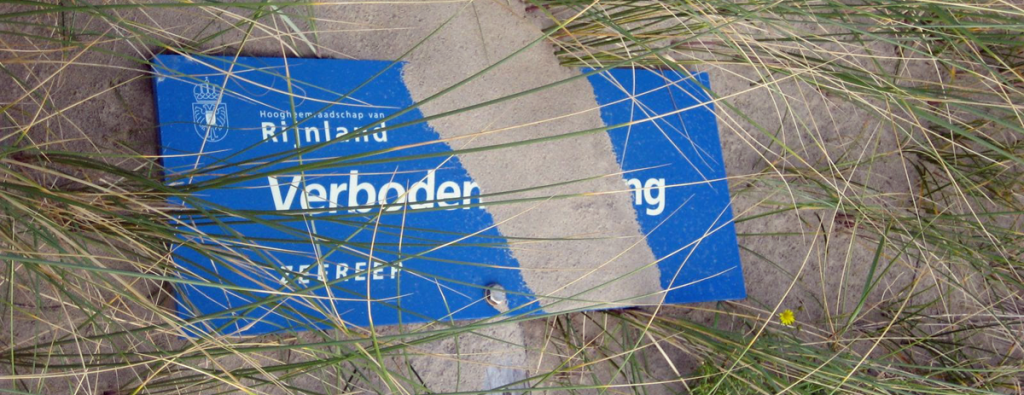 beeld toont een omgevallen "verboden toegang" bord in het duin